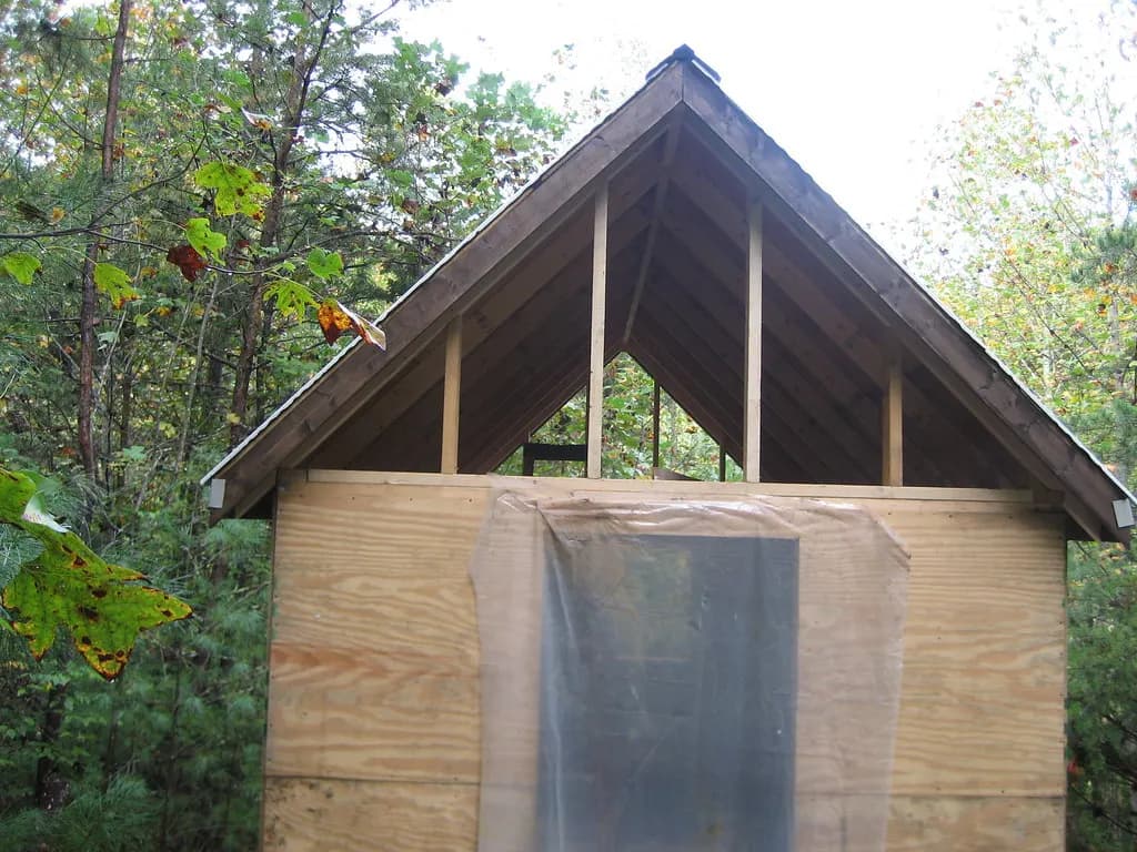 A small wood-framed building with an open gable end and plywood sheathing
