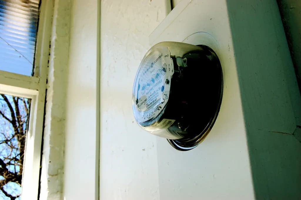 An electric meter mounted on the outside wall of a laundromat beside a window