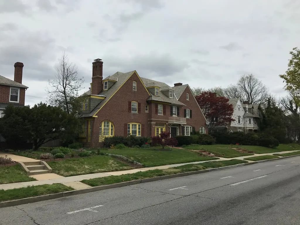 A large brick duplex house with two front entrances on a tree-lined residential street