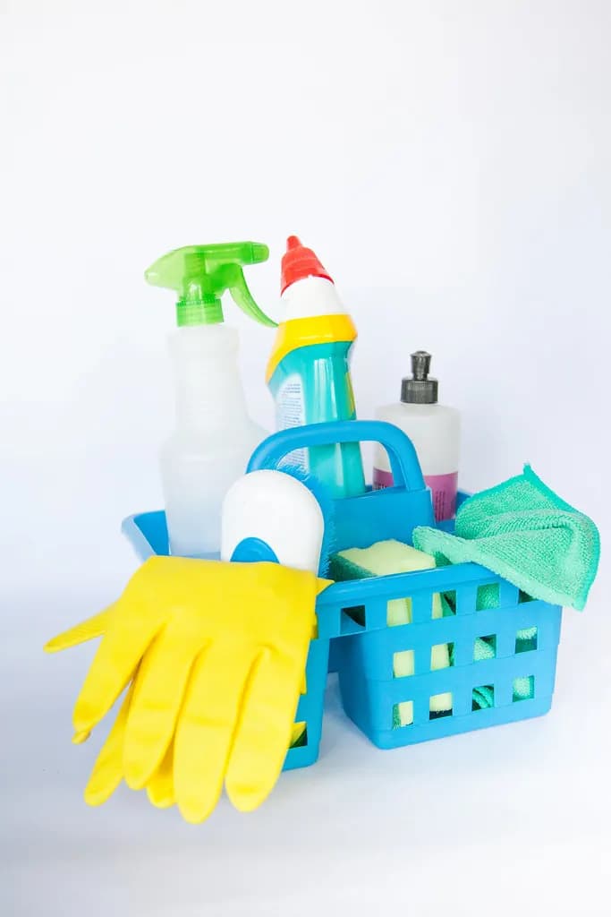 A blue cleaning caddy holding spray bottles, cleaning liquids, cloths and yellow rubber gloves