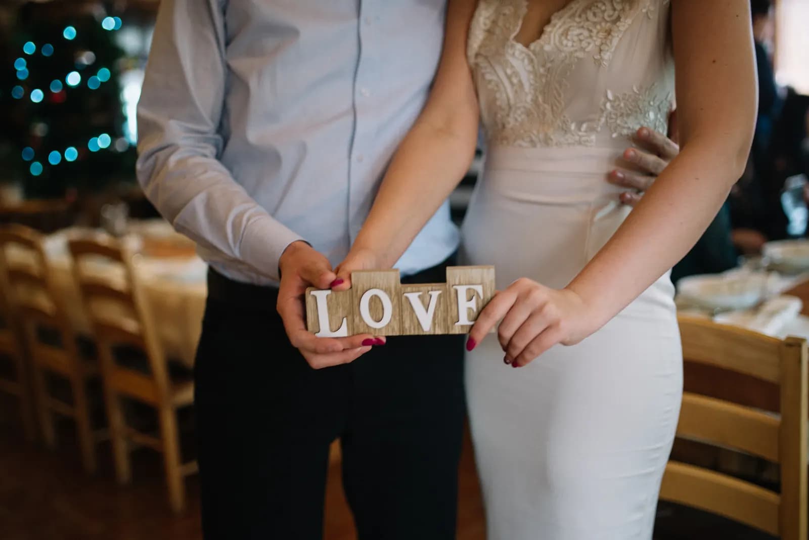 A bride and groom hold a small wooden LOVE sign at their decorated wedding reception venue