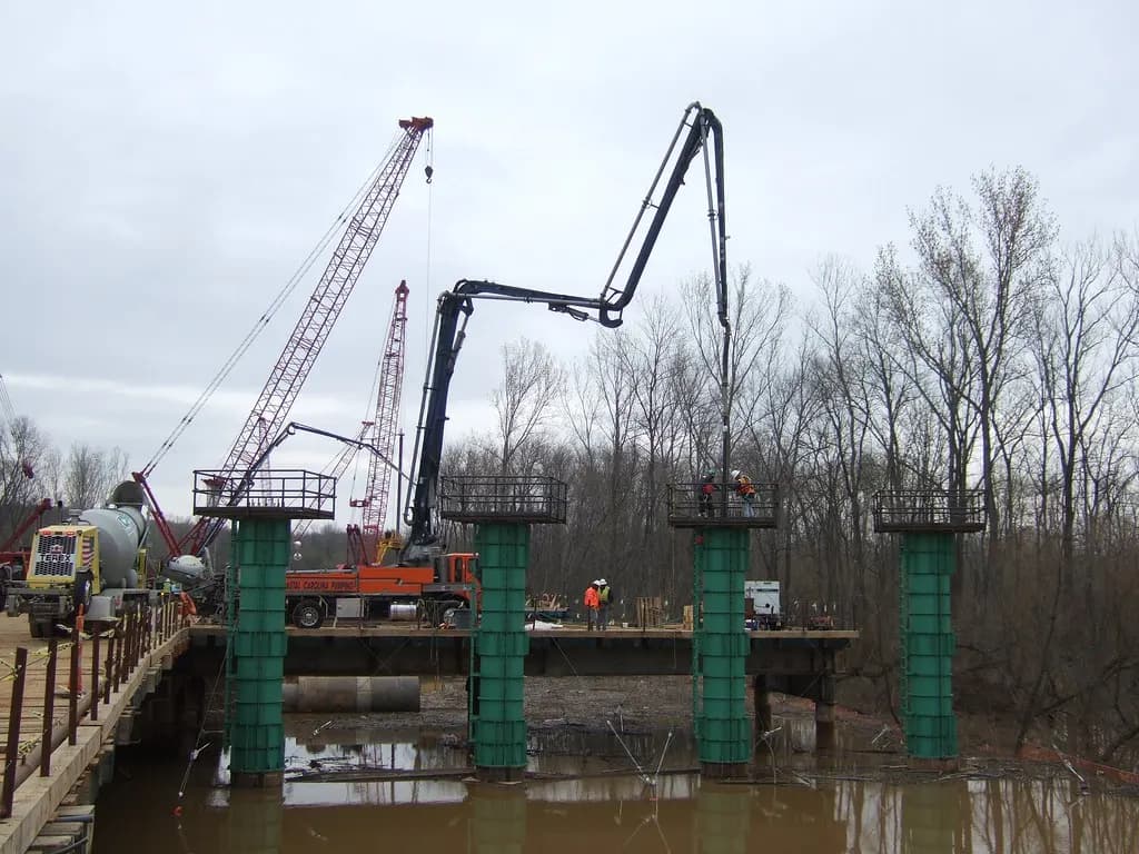 Cranes and a concrete pump building support columns for a highway bridge over a river