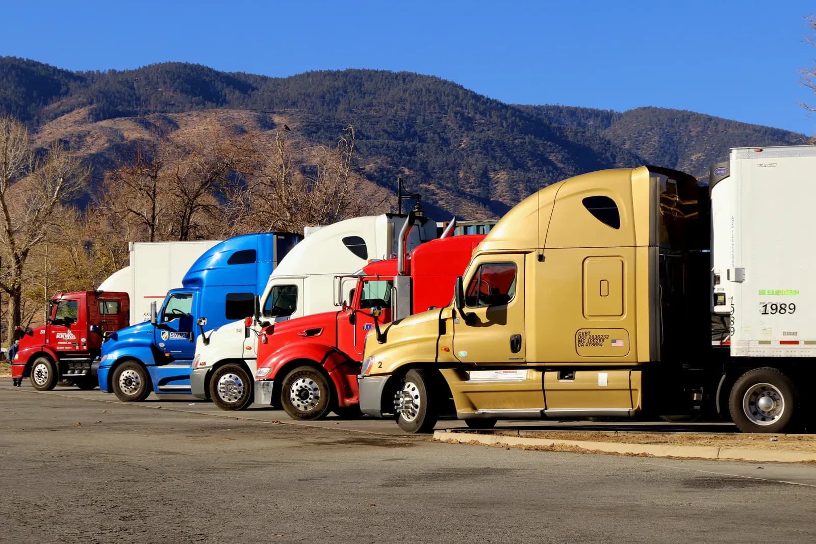 Row of colorful semi-truck tractors parked at a truck stop with mountains behind