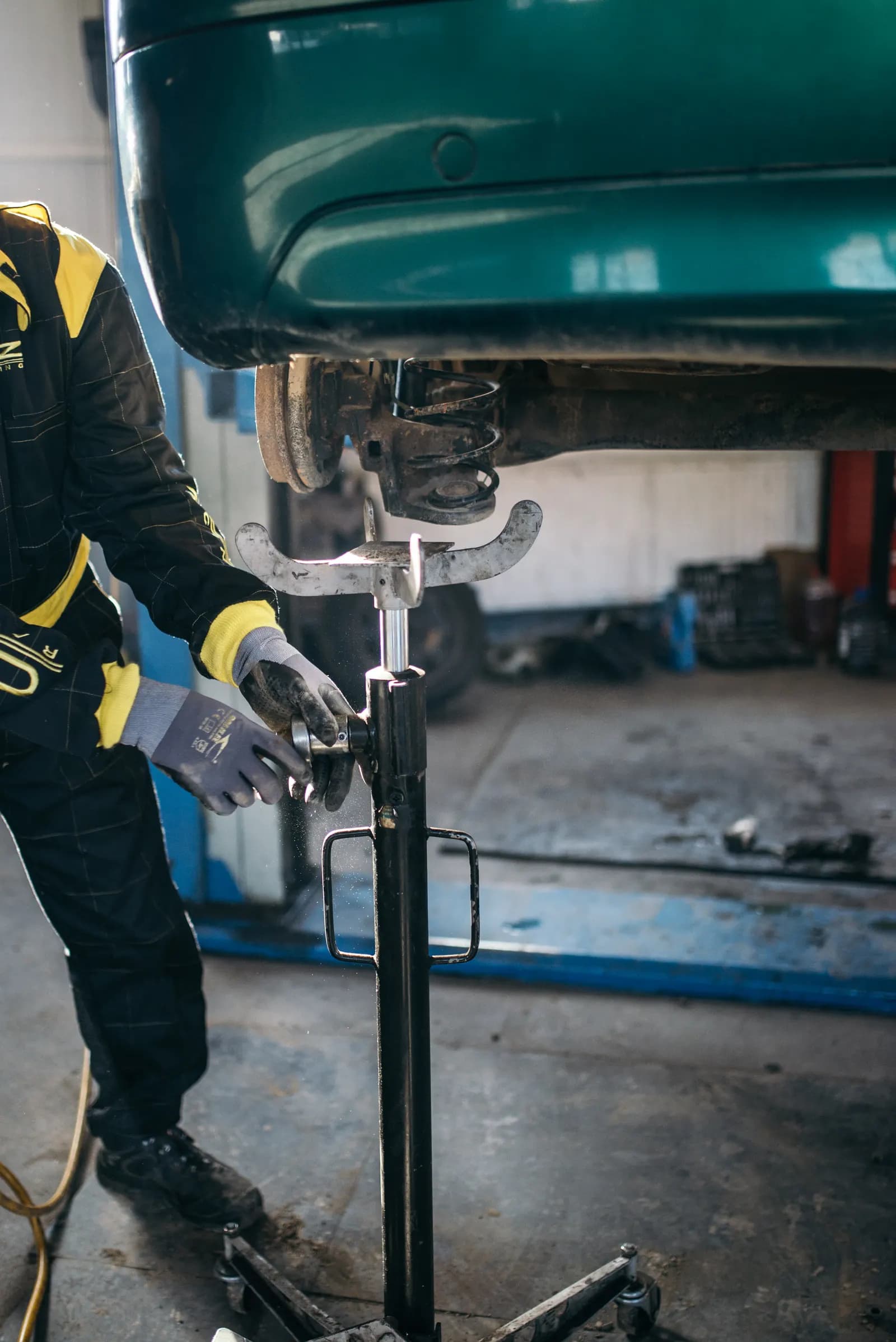 Mechanic in gloves using a transmission jack under a lifted car in an auto repair shop
