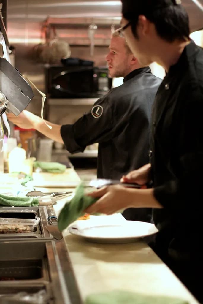 Cooks in black uniforms prepping food at a stainless steel restaurant kitchen station