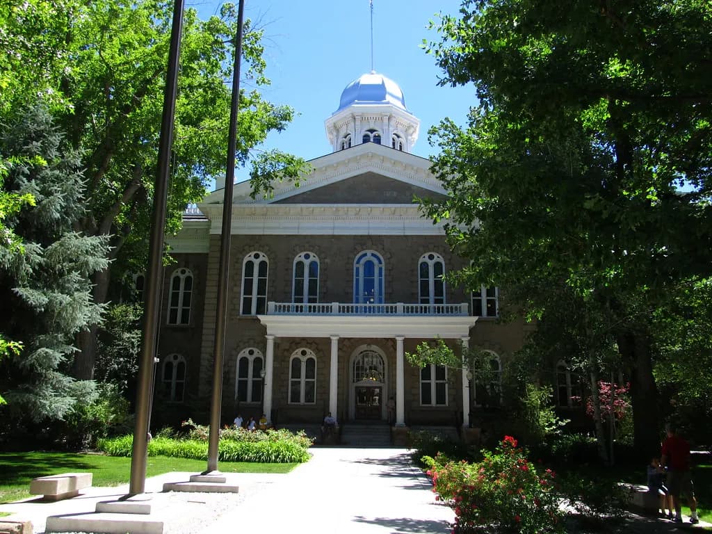 The Nevada State Capitol in Carson City, a sandstone building with a silver cupola, framed by trees