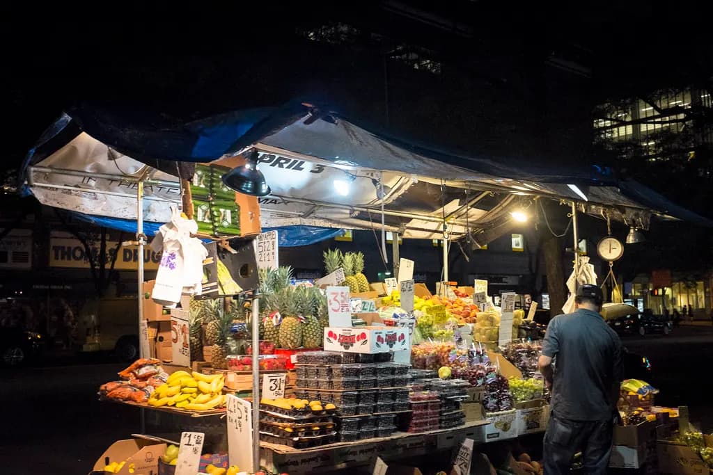 A street fruit cart stacked with produce on a New York City sidewalk