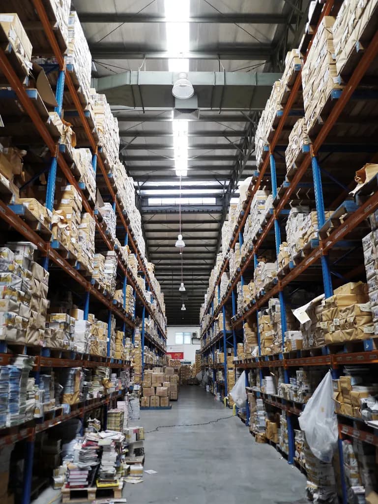 Long warehouse aisle lined with tall steel racking holding cartons of stock