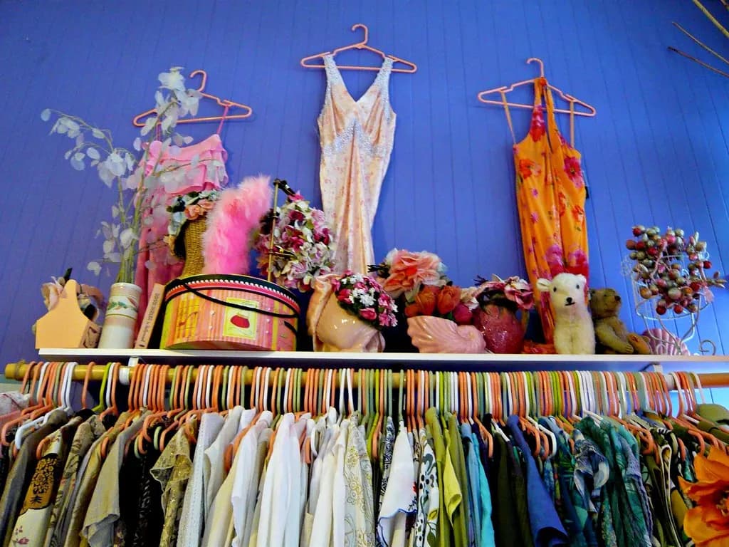A long rail of shirts and dresses on hangers in a clothing shop, with vintage dresses displayed above