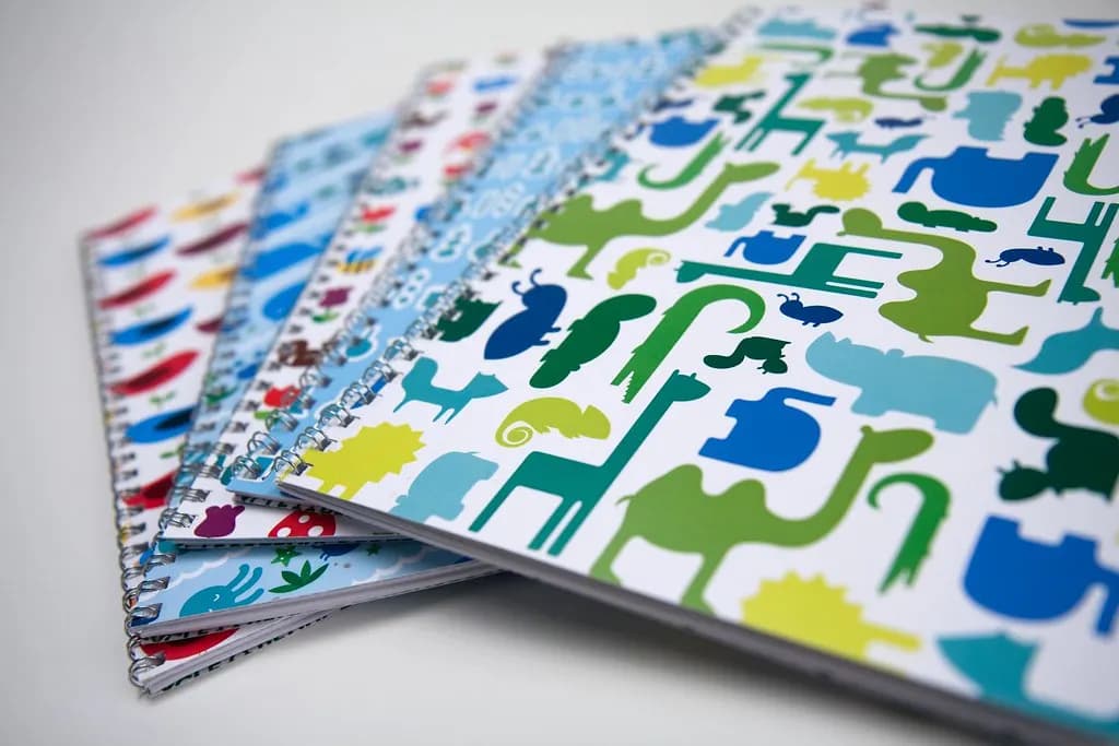 A fanned stack of spiral-bound school notebooks with colourful animal-pattern covers