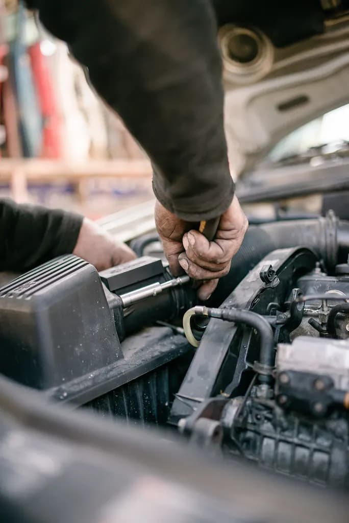 A mechanic leaning under the open hood of a car, working on the engine in a repair shop