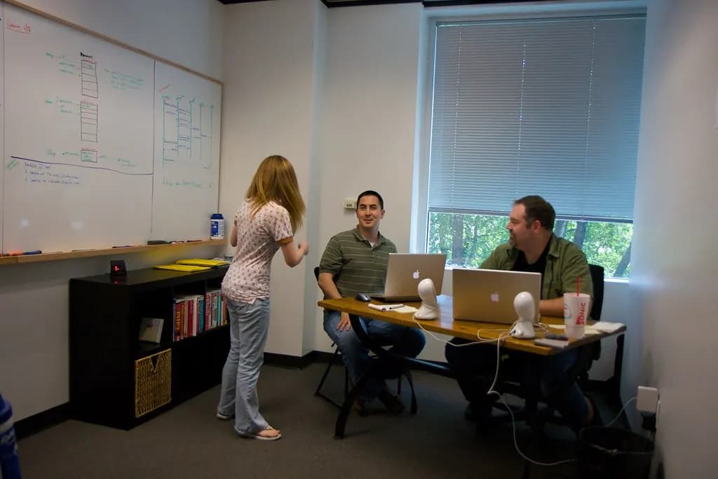A small web development team planning a project at a whiteboard with laptops on the table