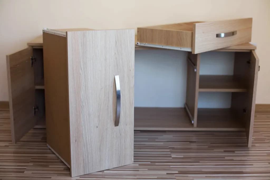 A newly delivered wooden sideboard with its doors and drawer open on a living room floor