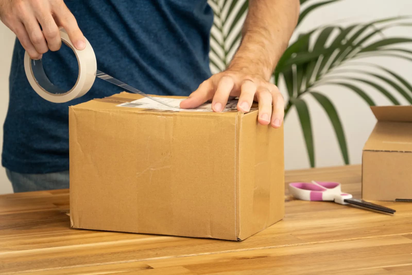Hands pressing a shipping label onto a cardboard parcel on a packing bench