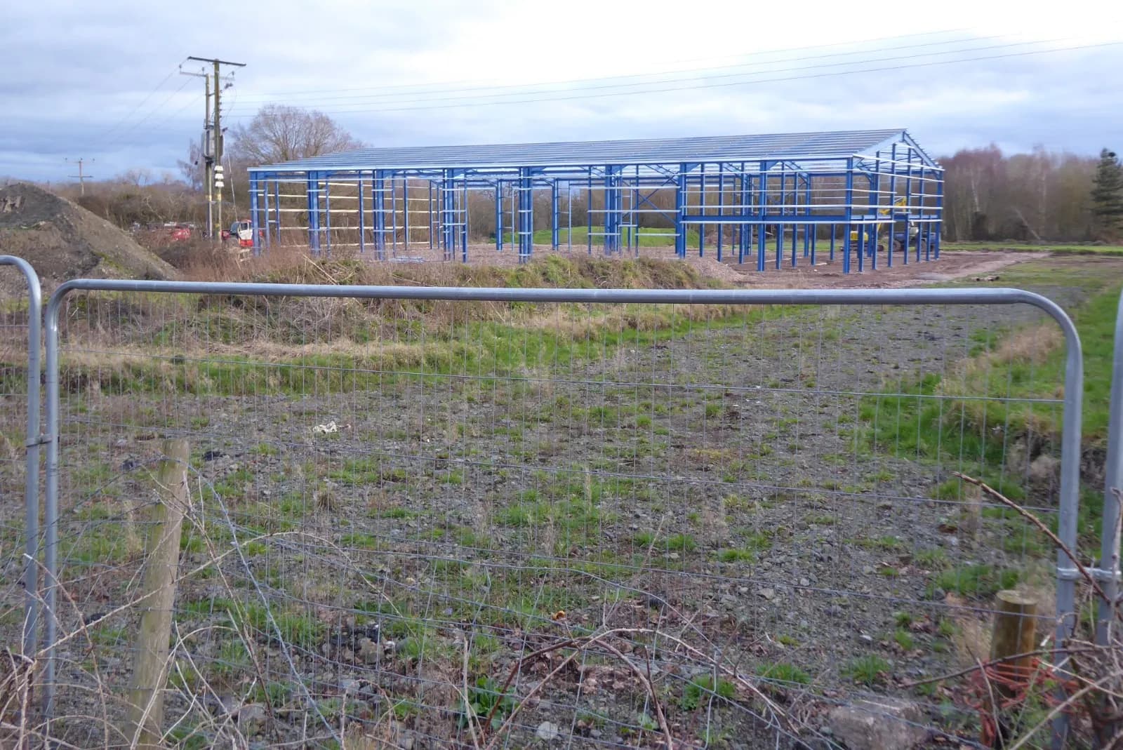 The blue steel frame of a new industrial building under construction on a cleared site