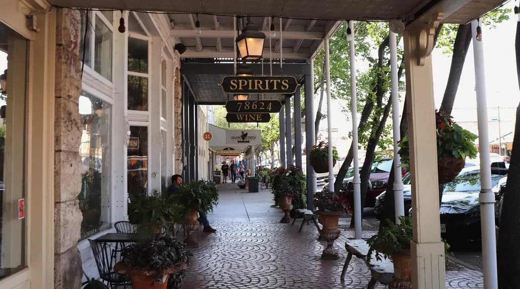 Covered sidewalk along Main Street in Fredericksburg, Texas, with planters, benches and shop doors